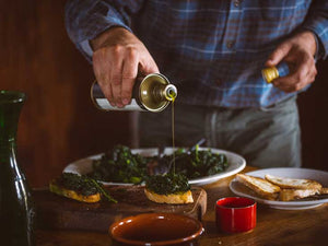 Extra virgin olive oil being poured from bottle onto salad